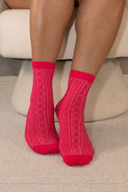 Bright pink crew socks with a textured cable-knit pattern, worn by a person sitting on a cream-colored chair.