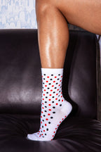 A person's leg resting on a black leather couch, wearing a white crew sock with a pattern of red and black polka dots.